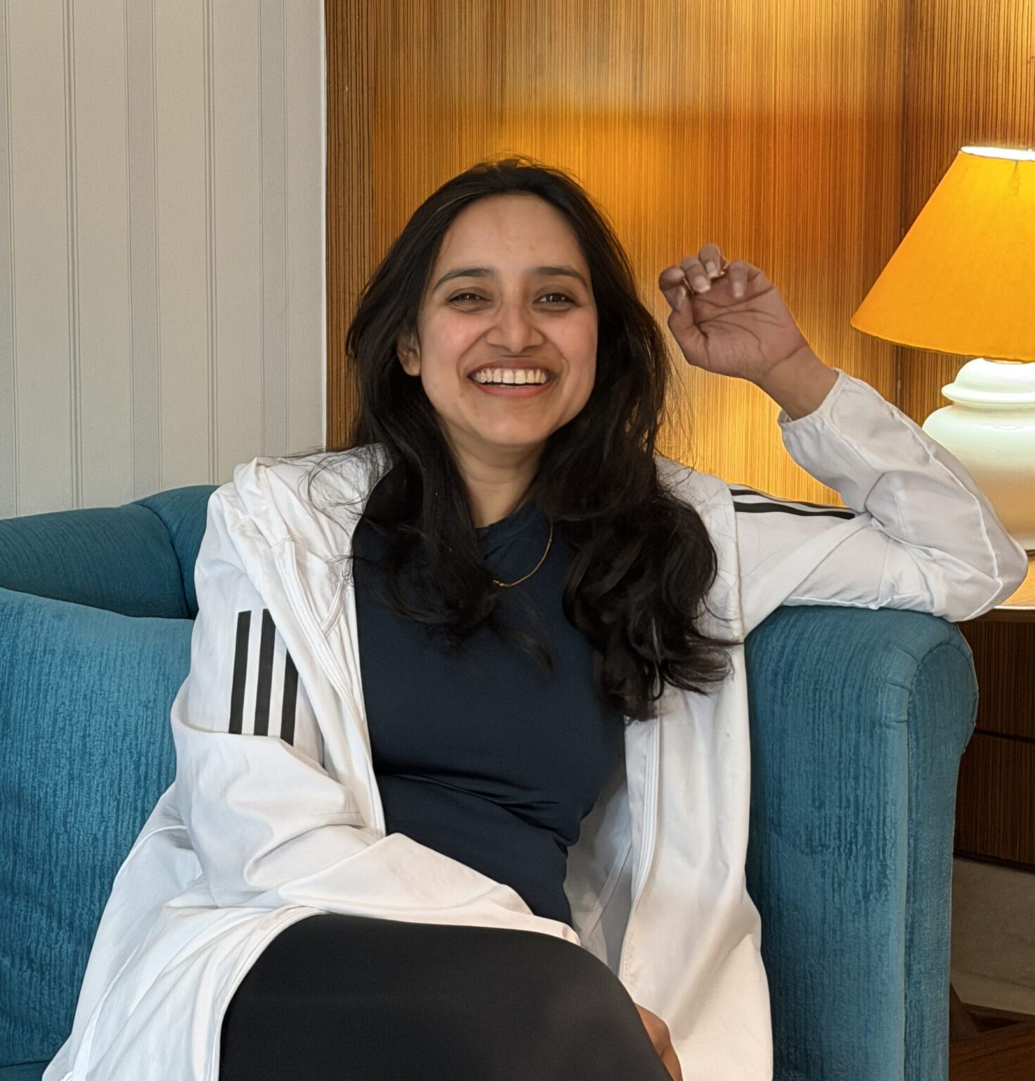 Smiling wellness coach in a white jacket seated on a teal couch